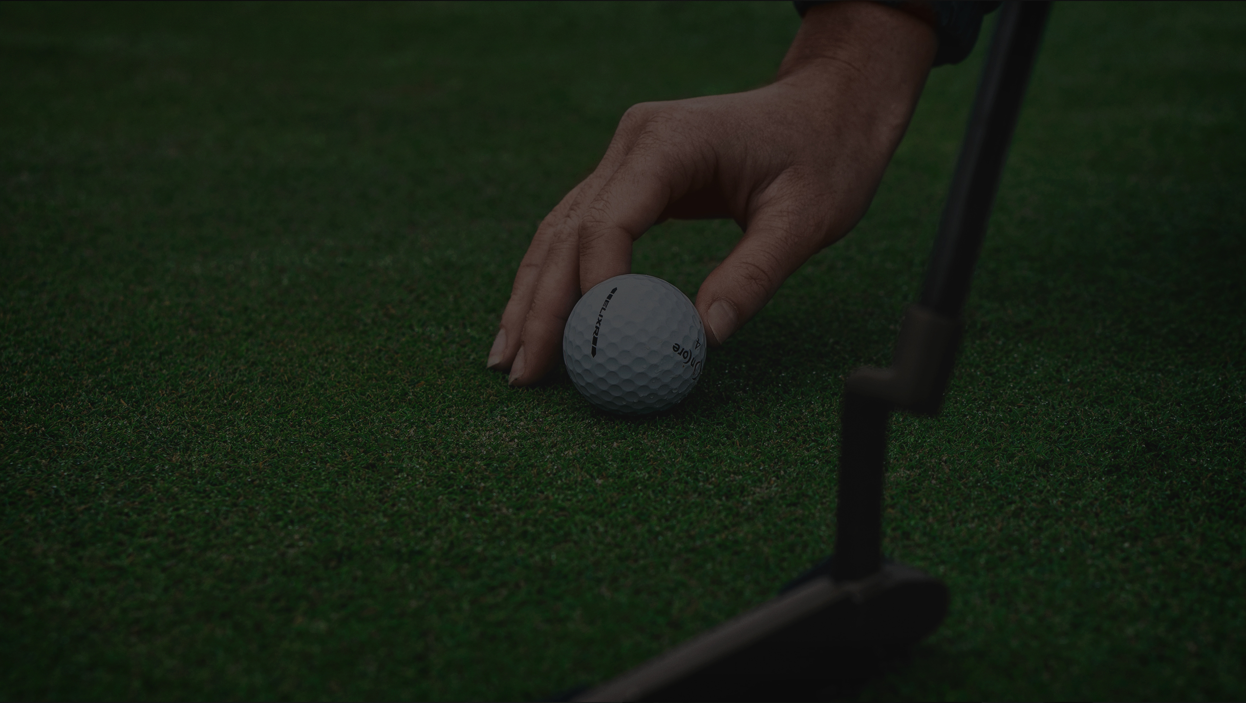 Hand replacing golf ball on green, next to putter