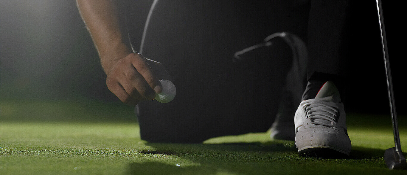 Golfer kneeling, pulling golf ball out of hole